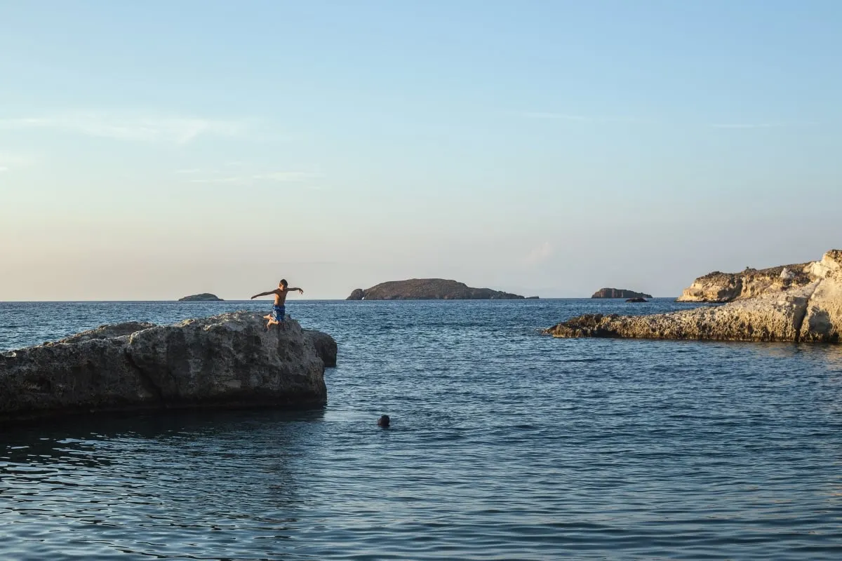Βραχώδης ακτή στο Κλέφτικο της Μήλου με τουριστικό σκάφος